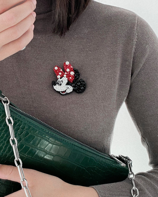 Person wearing a sweater with a Minnie Mouse beaded brooch, holding a green handbag.