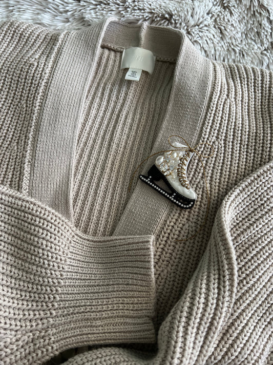 Close-up of a gray sweater with a ice skate brooch.