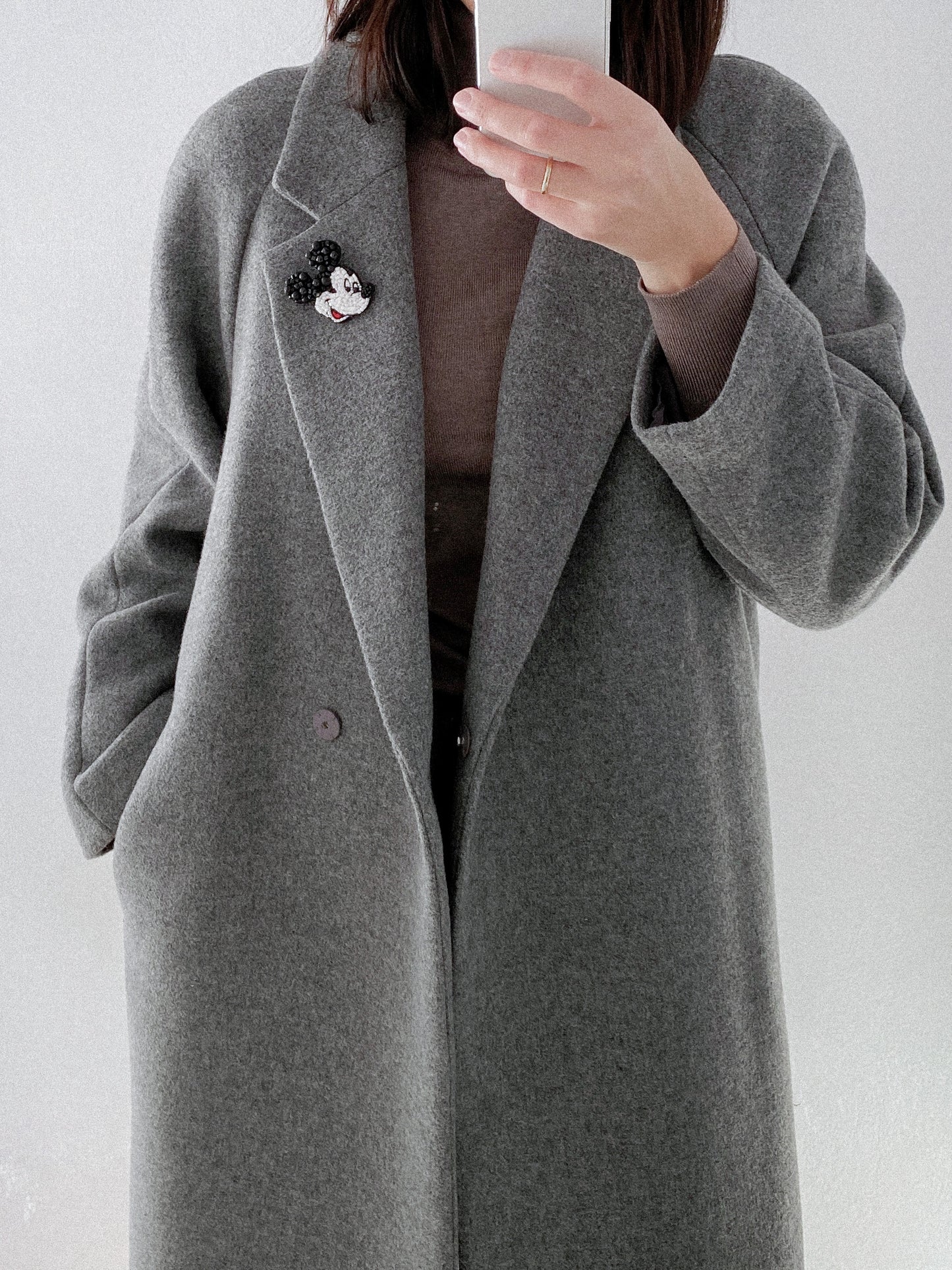 Person wearing a gray coat with a beaded Mickey brooch.