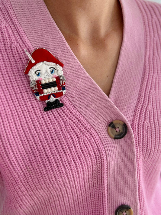 Big red Christmas Nutcracker soldier brooch on pink cardigan.