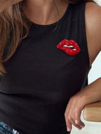 A close-up of a woman wearing a black ribbed tank top with a red beaded biting lip brooch pinned to the chest.