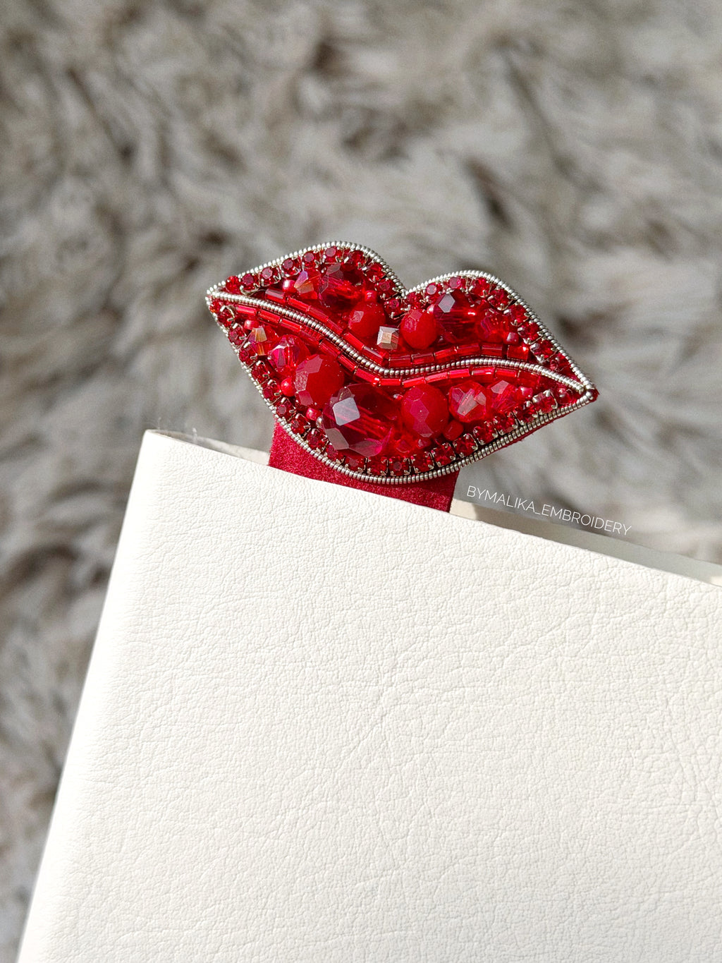 Red lip-shaped bookmark with gemstones on a textured surface
