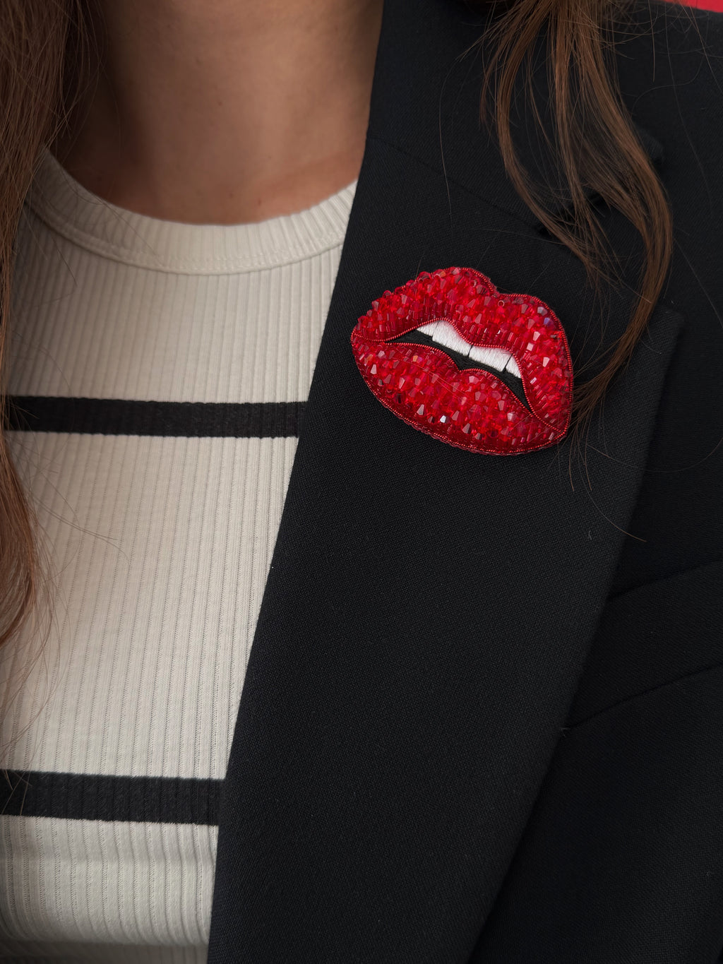 Black blazer with a red lip-shaped brooch worn by a person.