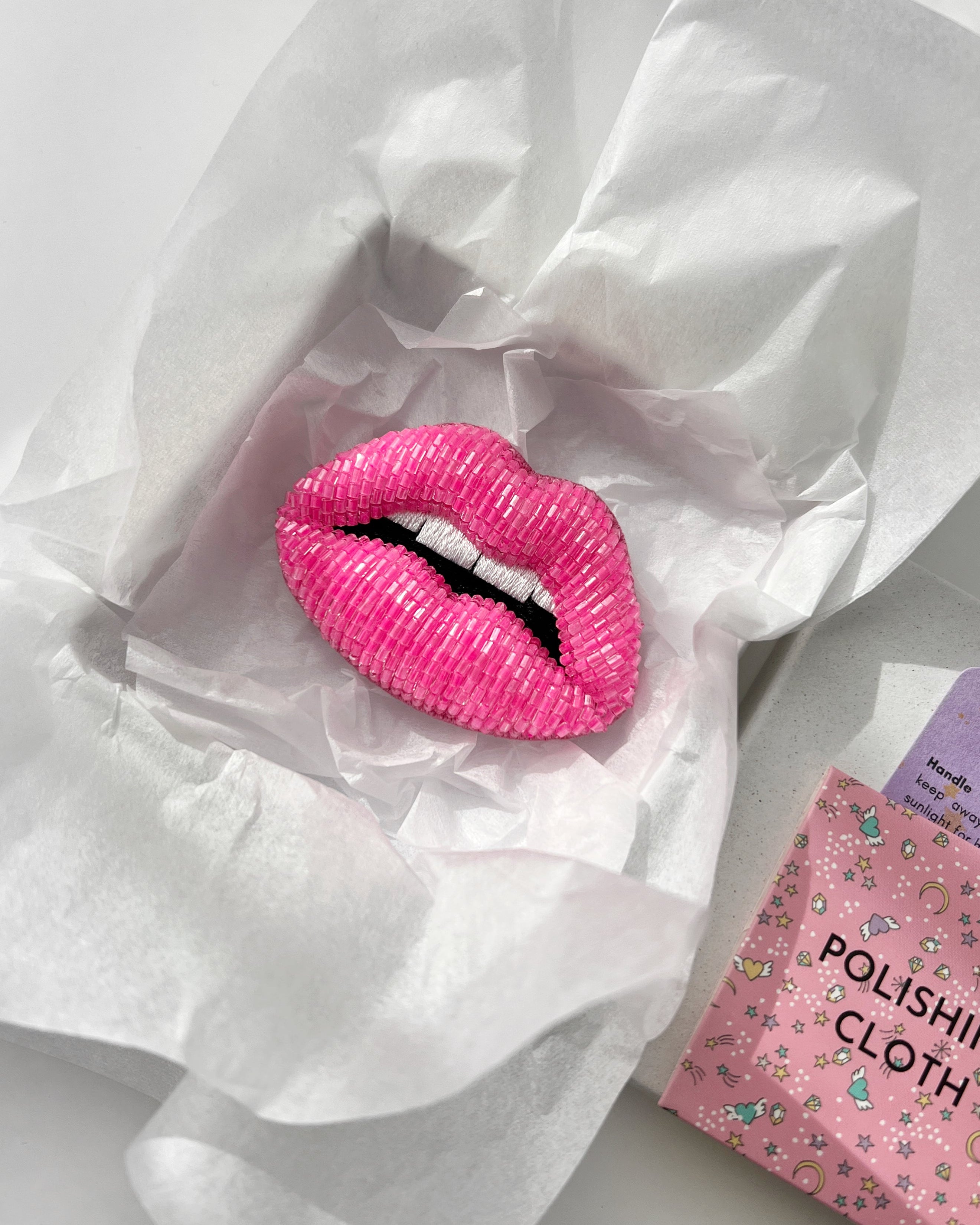 Hot pink seed beaded lip brooch packed in white by malika branded gift box with care card and polishing cloth.