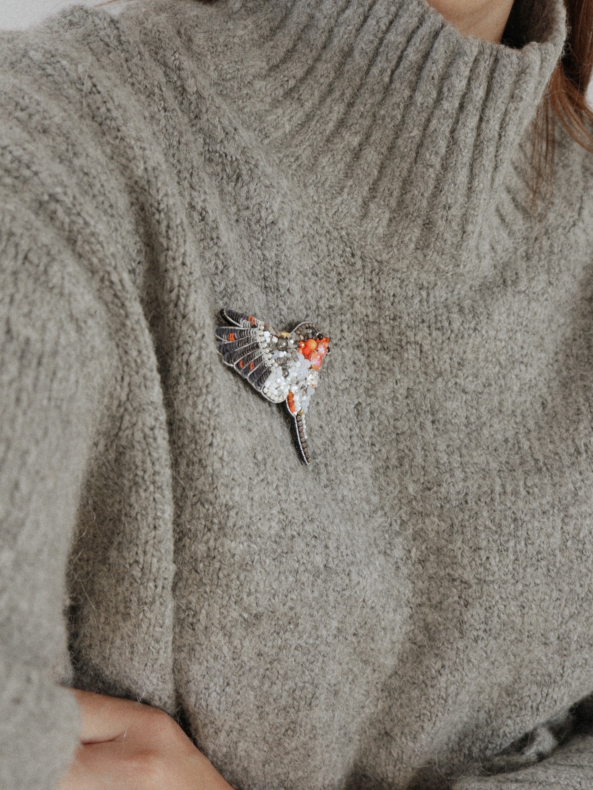 Close-up of a gray sweater with a beaded Robin bird brooch on the chest.