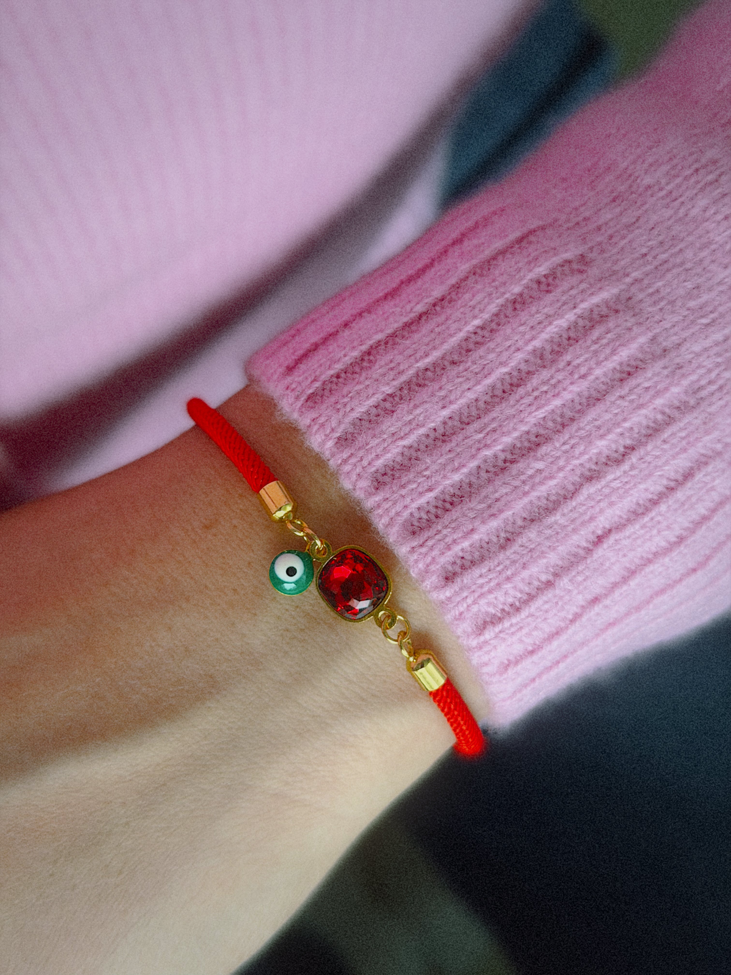 Red bracelet with gold accents and a red gemstone on a wrist against a pink sweater background