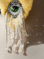 Yellow heart with eye in the center brooch design, beads, and chain fringe drop sparkle on a neutral background