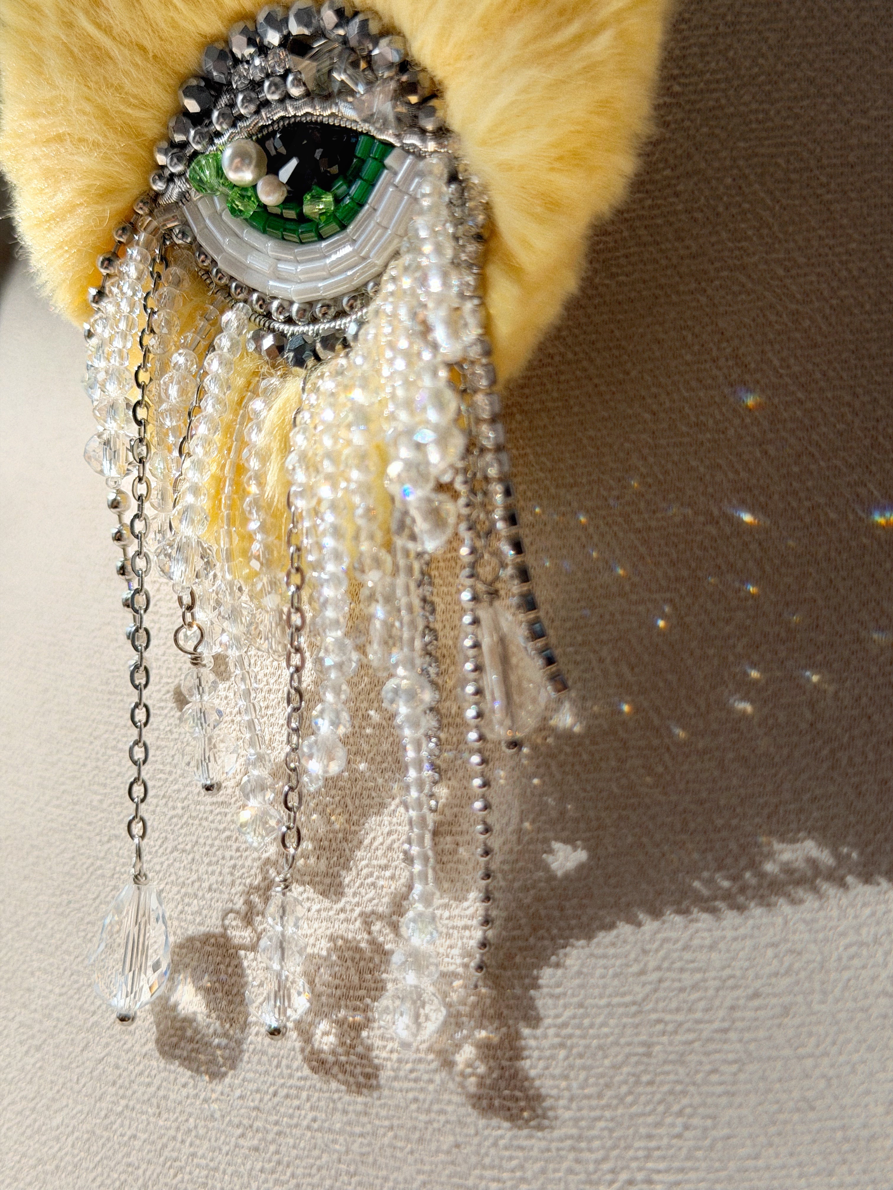 Yellow heart with eye in the center brooch design, beads, and chain fringe drop sparkle on a neutral background